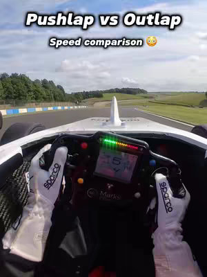 First-person view from inside a race car on a track. The driver's hands are on the steering wheel, which dominates the foreground. The track and scenery are visible through the windshield.