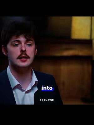 A man with dark hair and a mustache is centered in the frame, wearing a dark suit with a white dress shirt. The word "into" appears as a text overlay in a block of blue. The background is darkly lit, but there is an indication of a wooden wall. A website address is visible in the bottom.