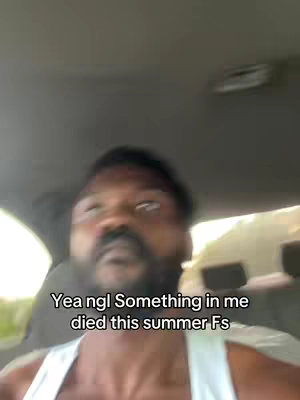 A selfie-style shot inside a car. A man with a beard is the central focus, blurred but clearly visible. The interior of the car is visible with the color of the car a neutral palette.