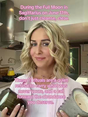 A woman with blonde wavy hair, pink top, and a gentle smile stands in a kitchen setting, holding two candles. Text overlays in pink and white describe rituals related to the Full Moon in Sagittarius.