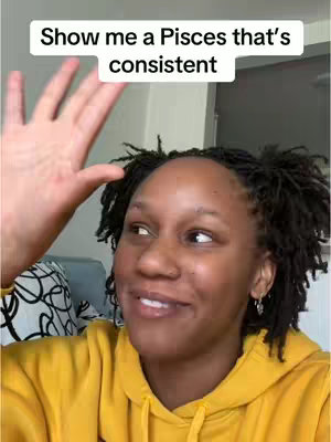 A head-and-shoulders shot shows a woman looking slightly off-camera with a hand raised. She has dark, short, styled hair and is wearing a yellow hoodie and earrings. A text overlay reads: "Show me a Pisces that's consistent."