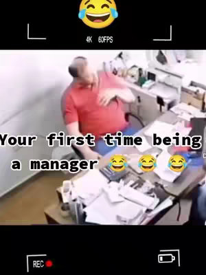 The image is a screenshot from a video, framed like a phone recording, showing a man sitting at a desk in what appears to be an office. The man, dressed in a red shirt, is the central figure. The top of the frame has a laughing emoji, and below that are the words "4K 60FPS." The text overlay at the bottom reads, "Your first time being a manager," followed by several laughing emojis. The office setting includes a desk with scattered papers and office supplies, adding to the casual, relatable feel.