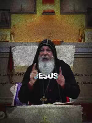 The image features an older man with a long white beard, wearing a black robe and a hood. He is sitting and gesturing with his hands, seemingly in a church setting. The word "JESUS" is superimposed over his chest in bold white text.