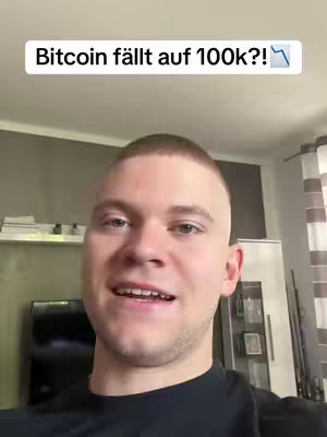 A young man with short hair smiles and speaks into the camera. Above his head, a rectangular text overlay reads, 'Bitcoin fällt auf 100k?!' with a downwards arrow. The background includes a glimpse of a room with furniture.