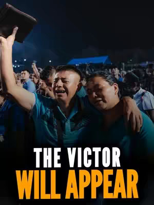 The cover image shows a crowd of people, most of whom are wearing blue shirts, filling what seems to be an outdoor event. In the foreground are two men; one is holding up a book, eyes closed, and the other has his arm around the first man's shoulder. The background is dark, suggesting the event is taking place at night, with a bright sky.