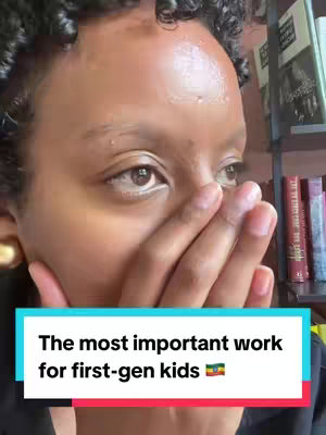 A close-up shot features a person, likely a woman, with their hand covering their mouth, creating a gesture of surprise or secrecy. The person has brown skin, curly dark hair, and is wearing gold earrings. The background is blurred, hinting at a room with bookshelves.