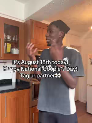 A man is standing in a kitchen setting, gesturing with his hands. Text overlays read, "it's August 18th today! Happy National Couple's Day! Tag ur partner <3". The kitchen has wooden cabinets and visible appliances in the background.