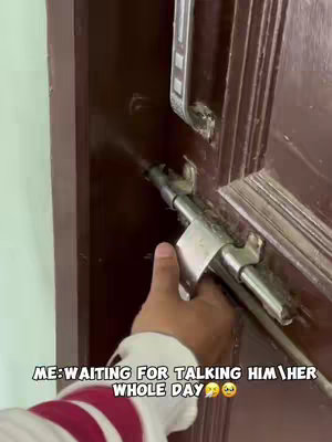 The image shows a hand partially visible, holding a door latch in the process of securing a wooden door. The hand is positioned on the right side of the frame, and the color of the door is dark brown.