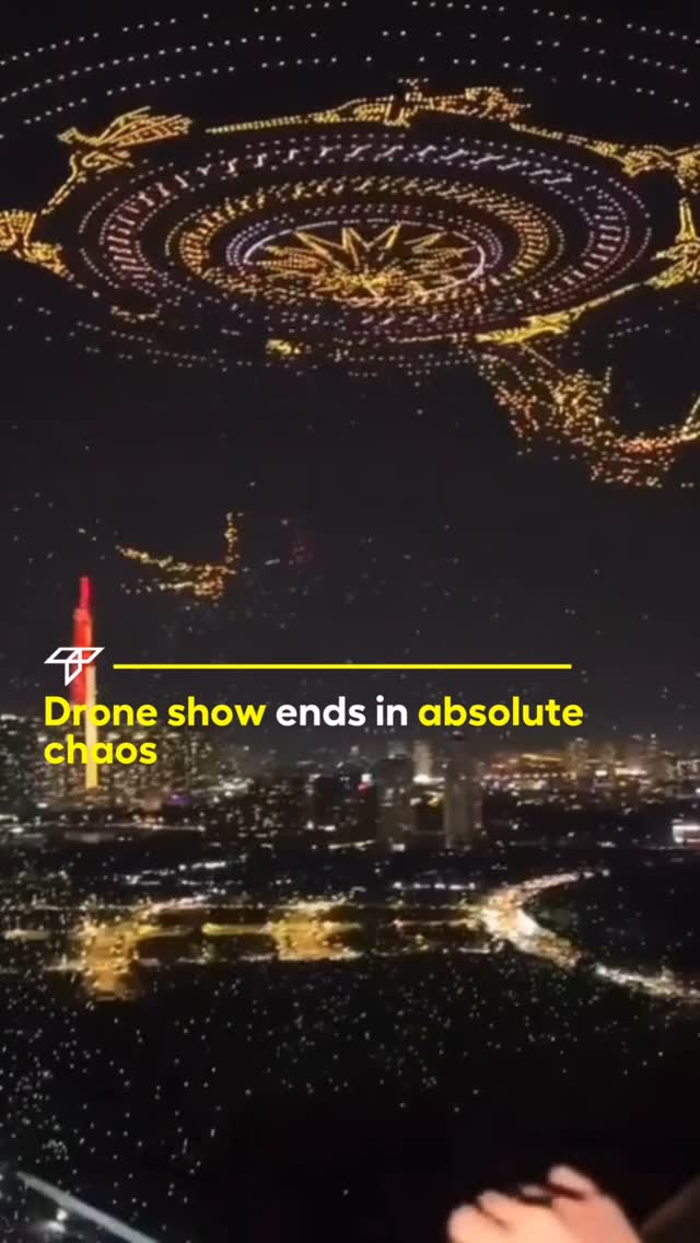 The cover image captures a nighttime aerial view, likely of a city skyline. A display of lights, likely from drones, forms a large, circular shape with a central star-like design and other scattered formations. The lower portion of the image shows the illuminated city, with visible buildings, streets, and lights. A yellow horizontal line cuts across the image, and is coupled with the overlaid text: "Drone show ends in absolute chaos".