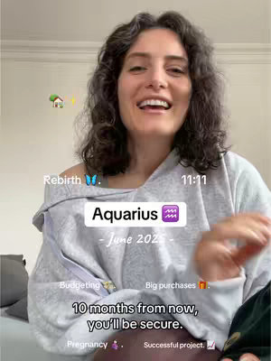 A woman with wavy dark hair is smiling broadly, looking towards the camera. She is wearing a light gray, off-the-shoulder sweater. Several overlaid text elements and small graphics are scattered across the image, including the word "Aquarius" in a white rectangle with a purple zodiac symbol, as well as text indications of the image's zodiac predictions.
