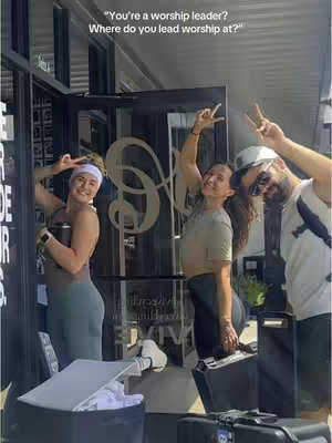 The cover image shows three young adults, two women and one man, posing outside a fitness studio entrance. The two women are on the left, both holding objects and flashing peace signs. The man is on the right, wearing sunglasses and also displaying a peace sign. The studio is visible behind them, the door is open.