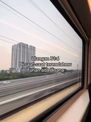 The image captures a view from a train window. The exterior presents a high-rise building in the distance, with a multi-lane highway in the middle ground and the evening sky as the backdrop. The text overlayed on the image has scripture-like content.