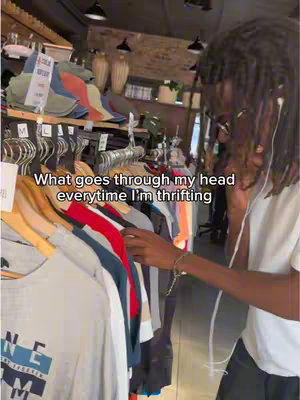 A person with dreadlocks and glasses stands in a thrift store, reaching for clothes on a rack. The scene captures a moment while thrifting. The text overlay states: What goes through my head everytime I'm thrifting. 
