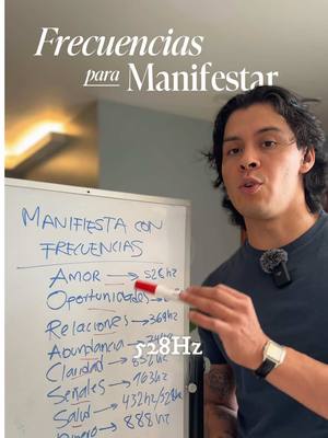 A man stands in front of a whiteboard and talks to the camera. The board has "Manifesta con Frecuencias" written on it with a breakdown of frequencies related to things like amor, oportunidades, relaciones and more. Text overlays on the image says "Frecuencias para Manifestar".