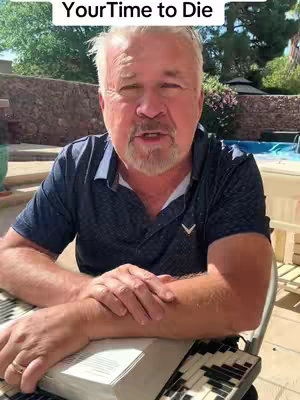 A man with white hair and a thick beard is outside, sitting in a chair with a book in his lap. In front of him is a stone wall and a pool, and the sky is visible at the top. Text overlaid reads "Your Time to Die."