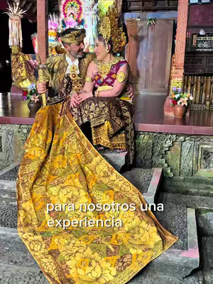 A couple in traditional Balinese wedding attire, smiling and embracing. The image is set against a backdrop of carved stone and intricate decorations, with added text overlayed on the bottom.