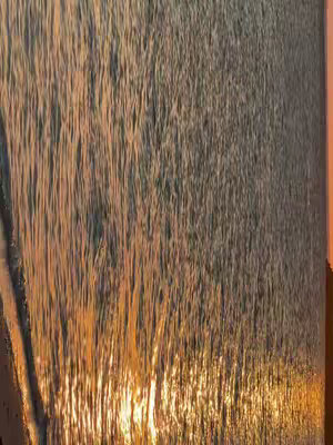 The cover image displays a close-up view of water, likely a waterfall or a fast-flowing stream, with sunlight reflecting off the surface. The colors are predominantly warm, with orange and golden hues indicating sunrise or sunset, while the rest of the image is colored in shades of gray and brown, creating a dynamic interplay of light and shadow. The composition is vertical, emphasizing the downward movement of the water.