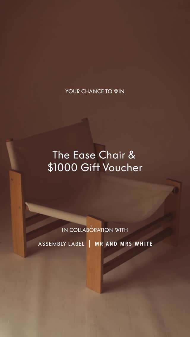 The image showcases a minimalist design, centered around a wooden chair with a white fabric seat. Text overlays mention a chance to win the chair and a gift voucher in collaboration with two brands.