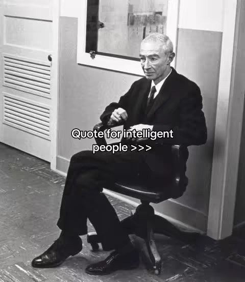 A black and white photo shows a man in a suit seated in a chair. He is looking towards the viewer.