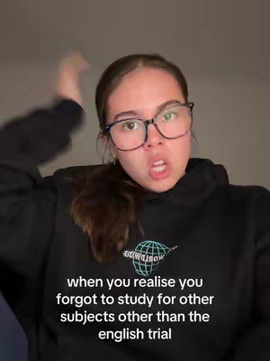 A young woman with glasses and a black hoodie is shown in a medium close-up. She is mid-expression, mouth open and one arm raised, positioned against a neutral background. Text is overlaid at the bottom of the frame.