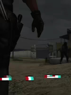 The image captures a scene from a video game, likely a third-person shooter, with a blurred background suggesting a desert environment. A figure's arm in a black glove and part of their tactical gear are visible on the left side, holding a firearm. In the background, a partial view of buildings and another figure adds context. The image has a muted color palette with dark tones, creating a sense of tension and potential action. At the bottom are some graphic details that provide a clue about video interface.