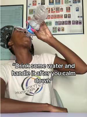 A person is holding a water bottle to their mouth to drink, with text overlaid on the bottom half of the image. They are wearing glasses, a bandana, and a white t-shirt. Behind them is a wall with various elements, including a large chart or poster.