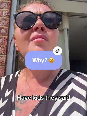 A woman wearing sunglasses looks towards the camera with a slightly pained expression. A speech bubble says "Why?" with a sad face emoji. Black and white striped top.