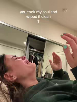 A woman is lying down, seen from a slightly upward angle. She appears to be emotional, with her mouth open wide as if she's crying or laughing, and her hands are raised in the air. The background includes a bedroom setting with a closet and a mirror. Text overlayed on the image reads, 'you took my soul and wiped it clean +.'