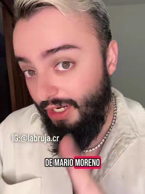 A close-up shot of a light-skinned man with a beard and short, styled blonde hair. He wears a white shirt and a silver chain. The man has a serious expression, with his mouth slightly open as if he is speaking. Text overlays are placed on the image.