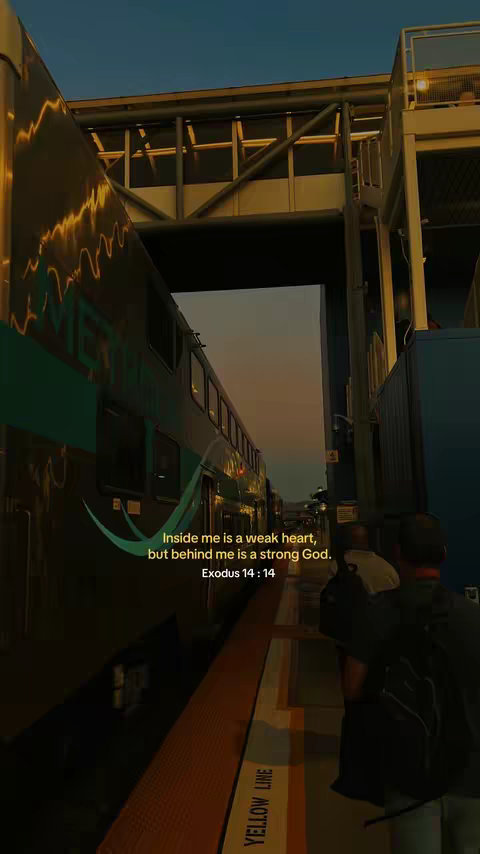The image shows a train platform scene at dusk. A train with dark teal and white carriages is on the left, with the word 'METRO' partially visible. In the center is a covered walkway over the platform, with a bright yellow line marked 'YELLOW LINE' on the platform. Two people are visible on the right. A person is walking in the dark under the walkway.