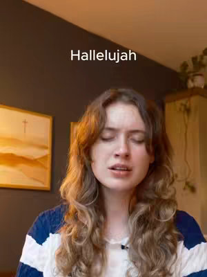 A woman with long, wavy brown hair is shown from the chest up, her eyes closed, and mouth slightly open as if she is singing. The background is a dark, solid color. Above her head is the text "Hallelujah" in white, sans-serif font.