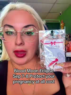 A woman with blonde hair and glasses is holding a packaged charm, with text on the image reading:
'Blood Moon Eclipse' and 'Sep 7-8 Protect your pregnancy at all cost'. She is looking at the camera with red lipstick.