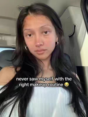A young woman with long black hair is centered in the frame, looking directly at the viewer. She has light skin, dark eyes, and is wearing small hoop earrings. The background is a blurry interior, possibly a car. Overlayed text sits near the bottom of the frame.