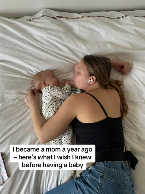 A woman and a baby are lying on a white bed, viewed from above. The woman is on the right side, with her head near the baby's, wearing a black tank top and jeans. The baby is dressed in a onesie with a polka dot pattern. Text is overlaid at the bottom, written in a rectangle. The overall composition suggests a moment of intimacy and rest.