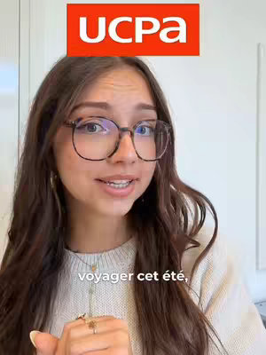 A young woman with brown hair and glasses is centered in the frame, talking with a slight smile. The UCPA logo in red is placed above her head. Text saying 'voyager cet été,' is at the bottom portion of the image.