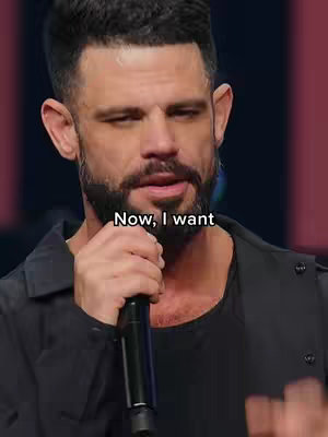 A medium shot of a man in a dark jacket, speaking into a microphone. Text overlay "Now, I want" at the bottom.