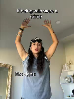 A young woman stands indoors with her arms raised, seemingly holding up an invisible object. She wears a gray tank top, jewelry, and a patterned bandana. Text overlays appear at the top and bottom of the image.