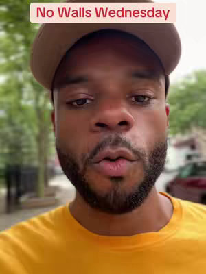 A selfie-style shot featuring a man wearing a brown cap and a yellow shirt. The text "No Walls Wednesday" is overlaid on the top. The background appears blurred, suggesting an outdoor setting, possibly a street or park.