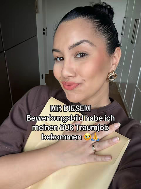 A selfie of a woman holding a folder, smiling at the camera, with text overlayed across the image. She has her hair up in a bun and is wearing gold hoop earrings and a brown shirt, against a background of simple built ins.