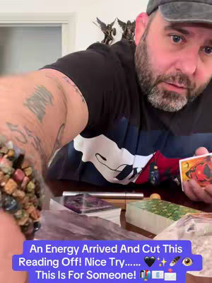 A man filming in a selfie-style, holding a deck of tarot cards. He is the primary focus, with a table and some decor in the background. Text overlay at the bottom of the image provides additional context.