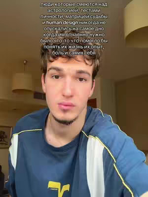 A selfie-style shot featuring a young man against an indoor backdrop. The man is the central focus, his face capturing most of the frame, implying a close-up or selfie perspective. He has short, dark hair and a light complexion. He's wearing a dark blue t-shirt with a yellow logo. The background is indistinct, with visible parts of a room, including light-colored walls and possibly ceiling lights. Overlayed in the image is text in Russian, which is partially obscured by the man's head.