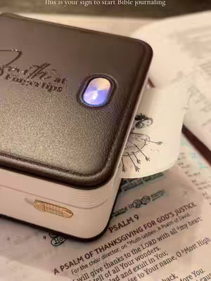 The cover shows a close-up of a brown leather-like device (likely a printer) with a glowing blue light in the center. Partially visible is a Bible open with pages and text from Psalm 9, with another sheet emerging from the printer.