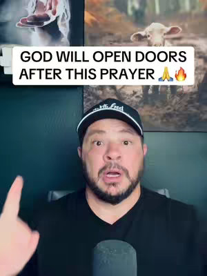 The cover image features a man with a beard and a black cap at the bottom of the image. He has an open mouth with a surprised expression and is pointing his index finger upward. The background includes some framed pictures. Superimposed over the image is a white rectangular box containing text that says "GOD WILL OPEN DOORS AFTER THIS PRAYER". A hand is pointing toward the top left. Two frames can be seen in the background. The overall image is bright and well-lit.