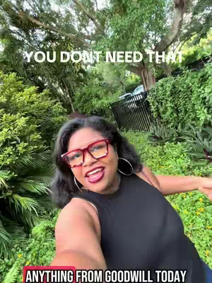 A woman with dark hair and red-framed glasses stands outdoors with a lush green background, smiling broadly and appearing to address the camera directly. Text overlays are present at the top and bottom of the frame, and she is wearing a black tank top.