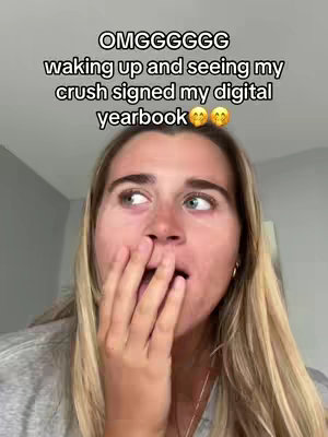 A close-up shot of a young woman with long blonde hair expressing surprise, her hand covering her mouth. Above her, text overlays indicate a significant, positive event involving signing a digital yearbook by her crush.