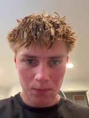 A close-up shot of a young man's face. He has wet, tousled hair and is looking directly at the camera. The background is a soft, out-of-focus interior.