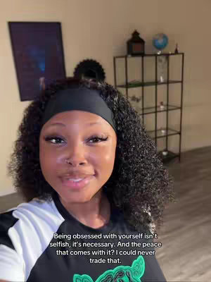 A selfie-style video cover image with a woman in the foreground. She is smiling slightly and has curly black hair. The background is a simple room with a cabinet and some decorations. There is overlaid text at the bottom.