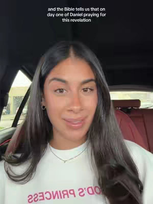 A woman with long, dark hair is the central focus, seated inside a car. She gazes towards the camera with a gentle expression, wearing a white sweatshirt. The background shows a view of a street outside, creating a sense of setting and personal space. Text overlays at the top add context.