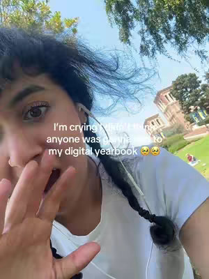 A selfie-style image shows a person, with a hand covering their mouth, likely reacting to the news. Additional elements include text overlay and a soft-focus outdoor background. The overall color scheme is natural with hints of green and blue.