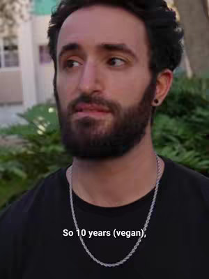 A close-up shot of a man with a beard and a silver chain, looking slightly off-camera. Text overlayed at the bottom reads, 'So 10 years (vegan)'. The setting appears to be outdoors with blurred greenery in the background.
